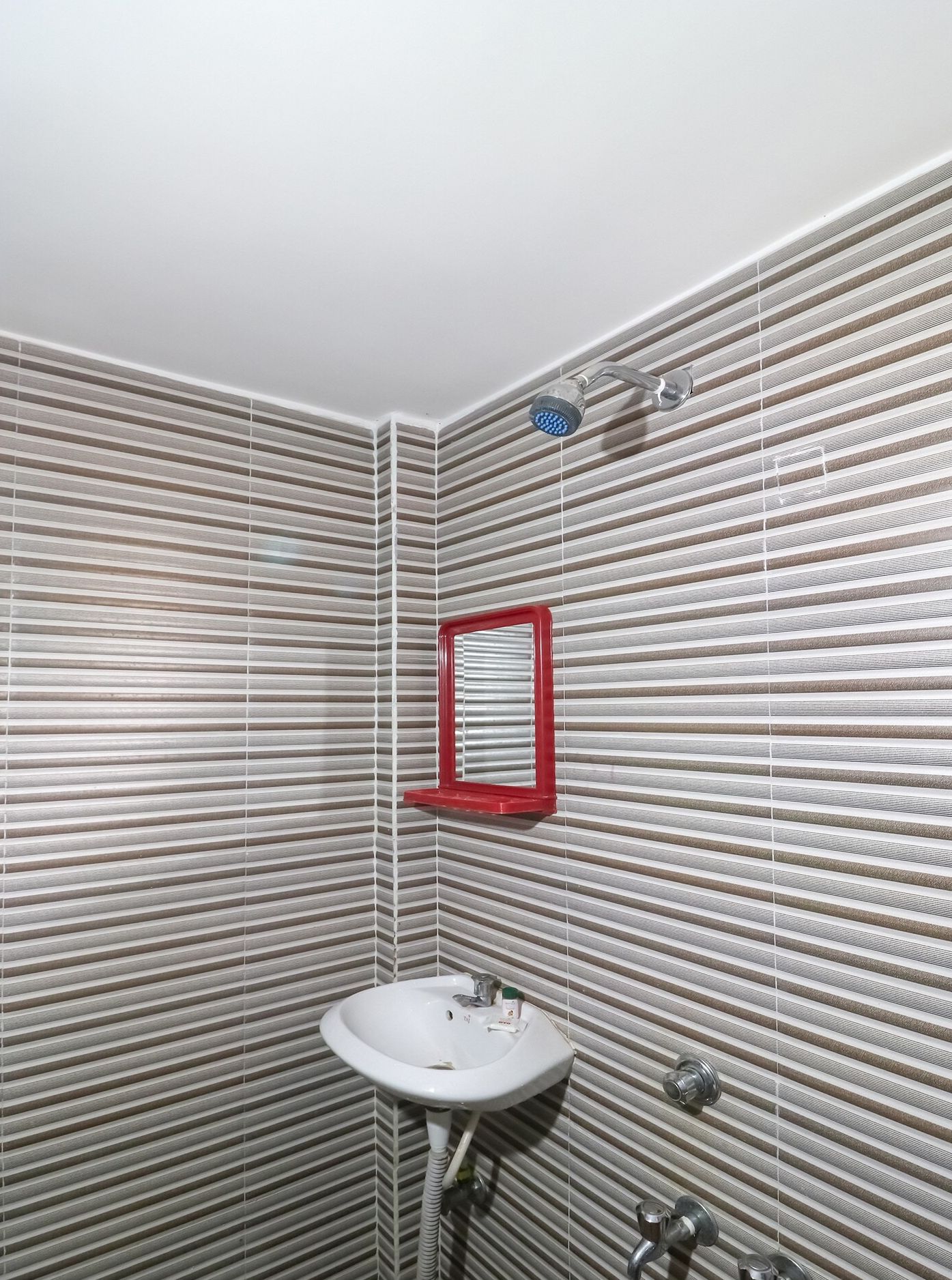 A bathroom with a striped wall pattern, a white sink, a red-framed mirror, and a showerhead.