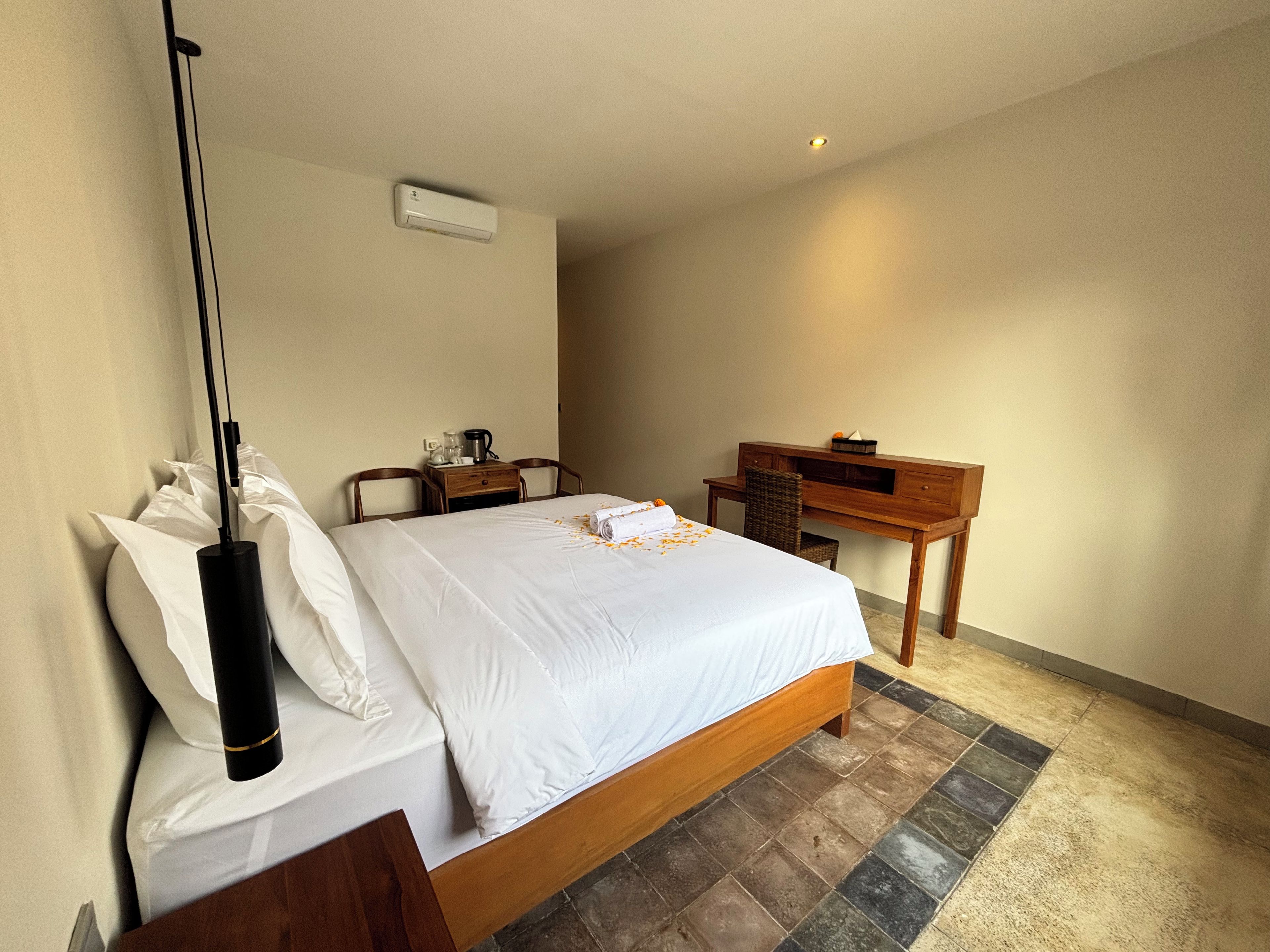 Een hotelkamer met een bed, nachtkastje, bureau, stoel en een airconditioning.