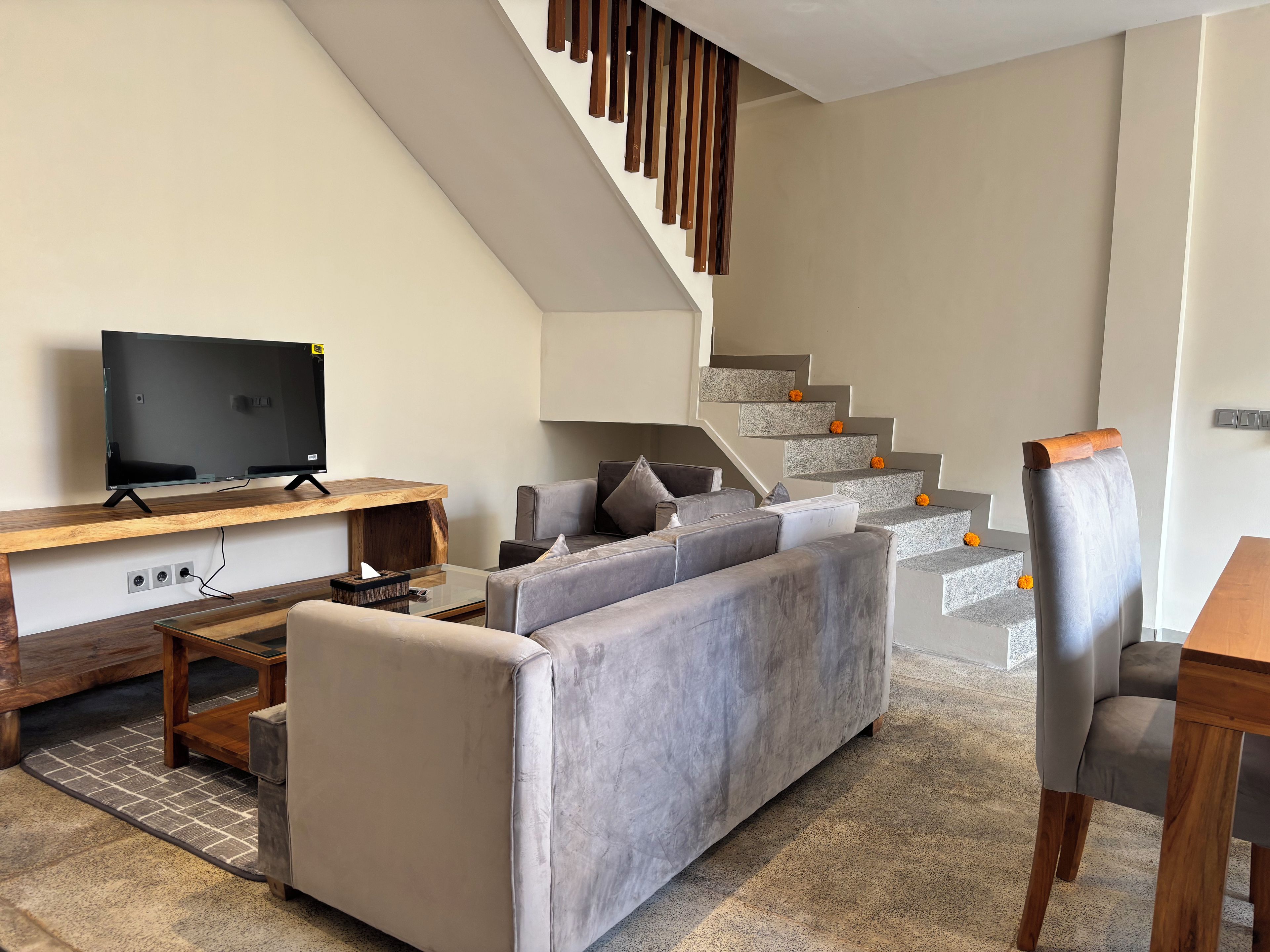 Een moderne woonkamer met een flatscreen televisie, een grijze bank, een houten salontafel en een trap versierd met oranje pompoenen.