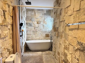 Un baño con pared de piedra, bañera, ducha e inodoro.