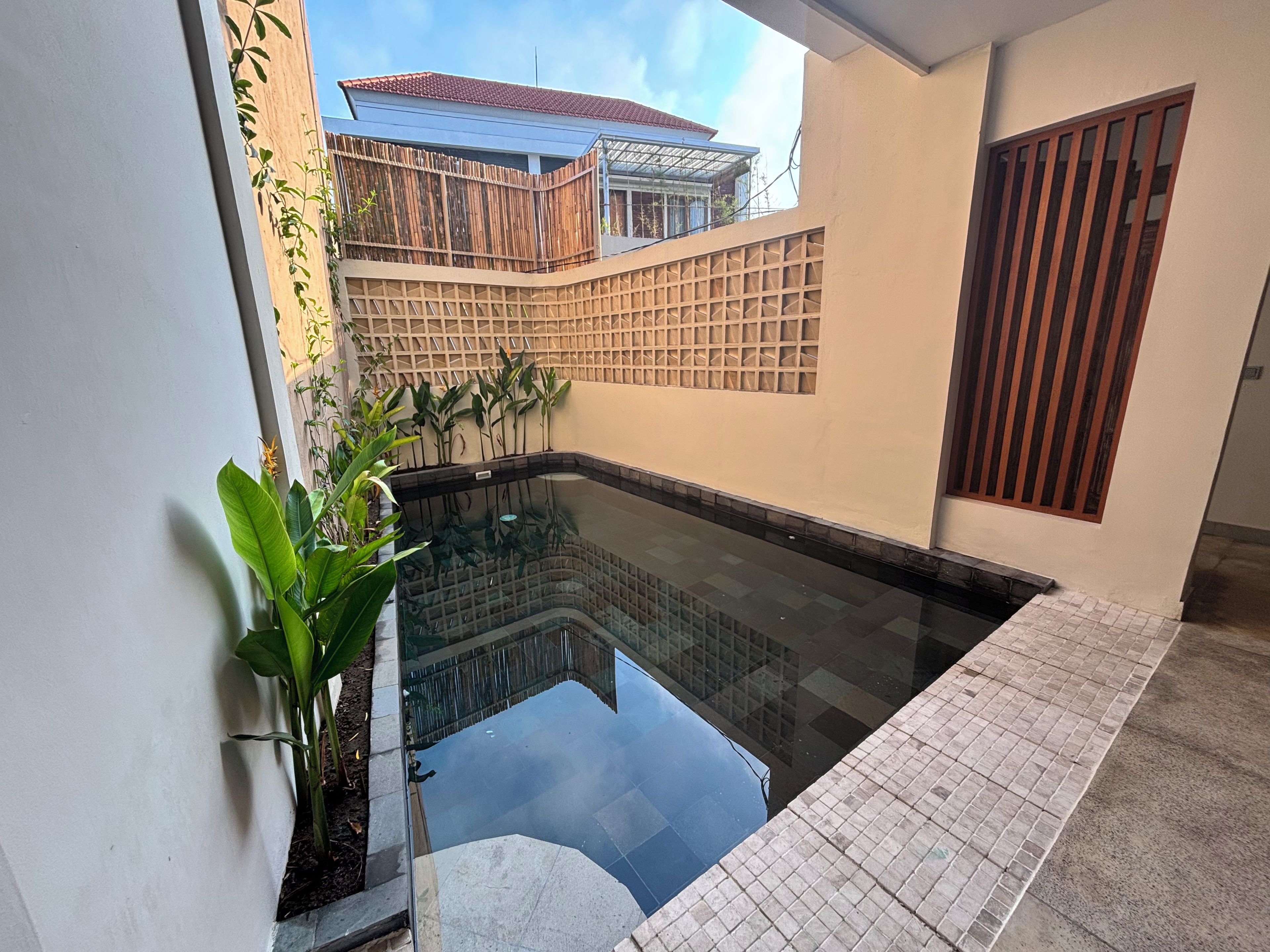 A swimming pool with a tiled deck, surrounded by walls with a geometric pattern, and a view of a neighboring building.