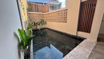 A swimming pool with a tiled deck, surrounded by walls with a geometric pattern, and a view of a neighboring building.