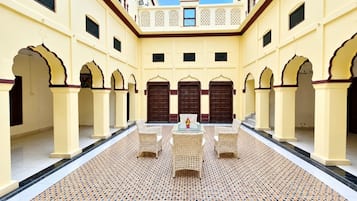 A courtyard with a central seating area, surrounded by arches and doors, under a clear sky.