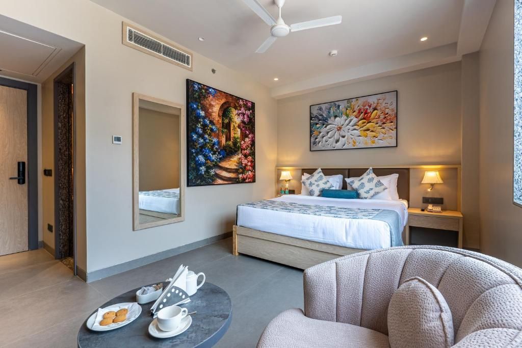 A hotel room with a bed, bedside tables, a round coffee table with breakfast items, and artwork on the walls.