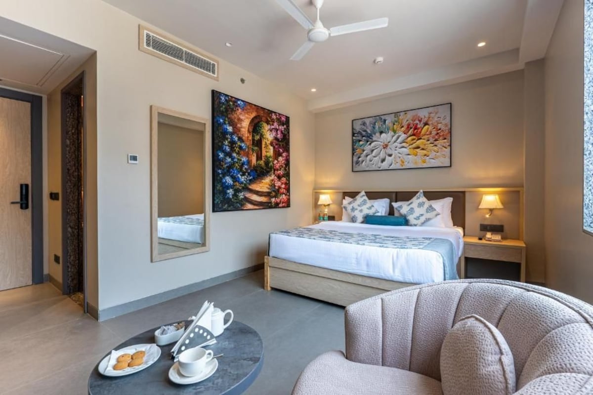 A hotel room with a bed, bedside tables, a round coffee table with breakfast items, and artwork on the walls.