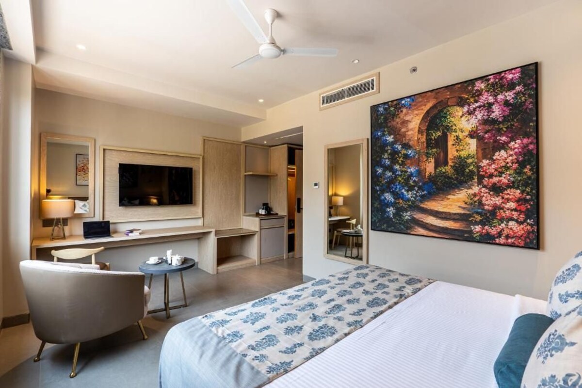 A hotel room with a bed, a desk, a chair, a TV, and a painting.