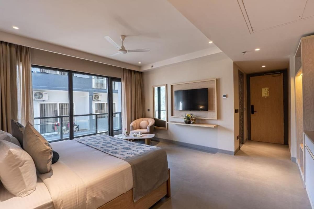 A hotel room with a bed, a TV mounted on the wall, and a balcony with a view.