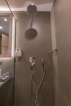 Zona de ducha con cabezal de ducha de mano, grifo empotrado en la pared y repisa de vidrio con artículos de aseo.