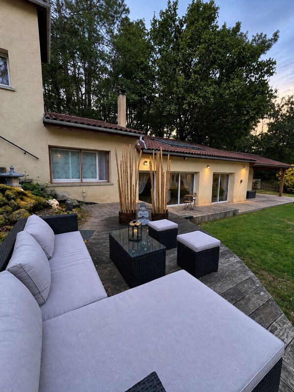 Una casa moderna con un patio que incluye un sofá, dos mesas cuadradas y una estatua de Buda.
