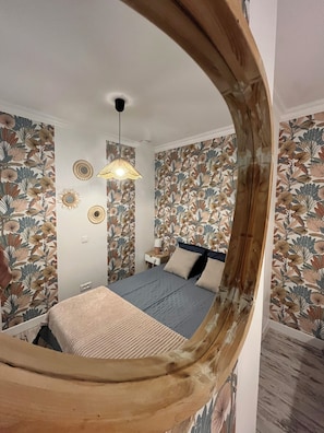 Un dormitorio con una cama, una mesita de noche, una lámpara y papel tapiz con motivos florales.