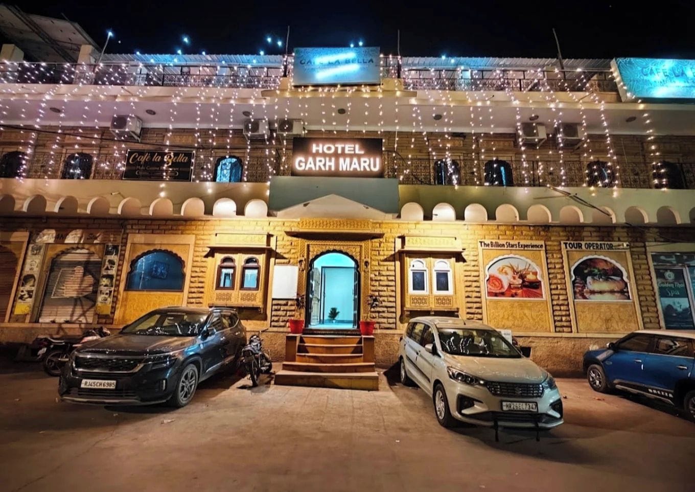 L'ingresso di un hotel con un cartello che riporta 'HOTEL GARH MARU', una scalinata che conduce all'entrata e auto parcheggiate di fronte.