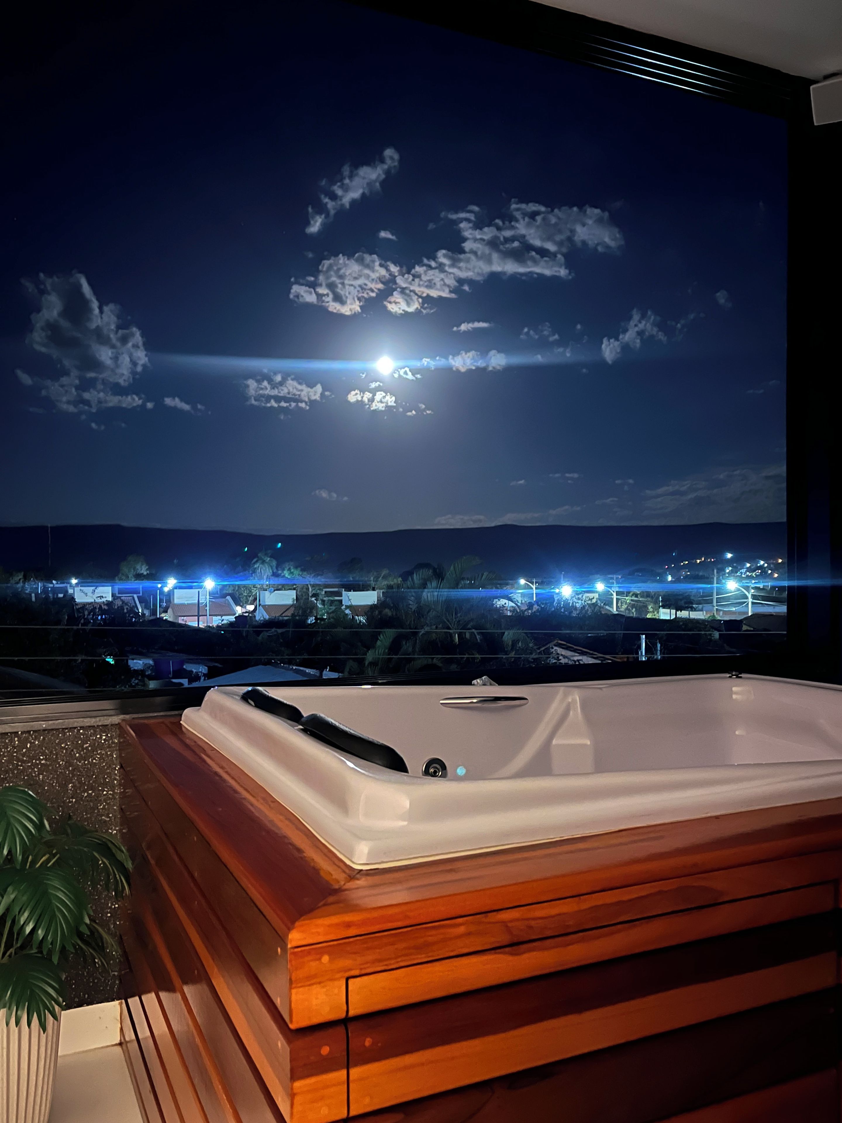 Un jacuzzi en una terraza de madera con vista a la ciudad de noche.