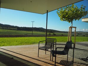 An outdoor seating area with two chairs and a table, a tree, and a view of a green landscape. - Apartment '1 EG Ost' with Private Terrace, Private Garden and Wi-Fi (Bad Dürrheim)