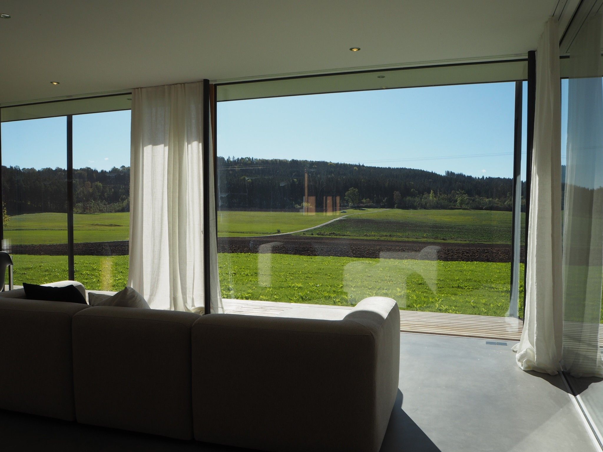 Een moderne woonkamer met een groot raam dat uitzicht biedt op een groen veld en bos.