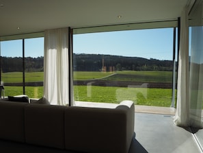 Een moderne woonkamer met een groot raam dat uitzicht biedt op een groen veld en bos.