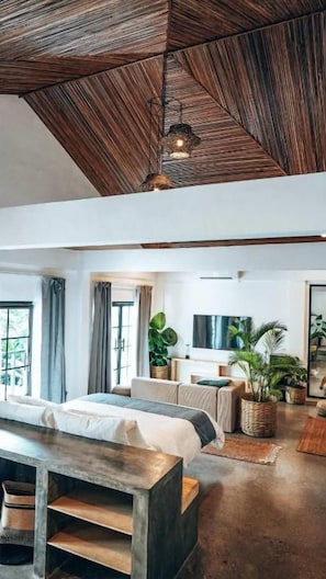 A spacious room with a high ceiling, a bed, a wooden table, and a television. - Bliss villa by Happiness Philippines (El Nido)
