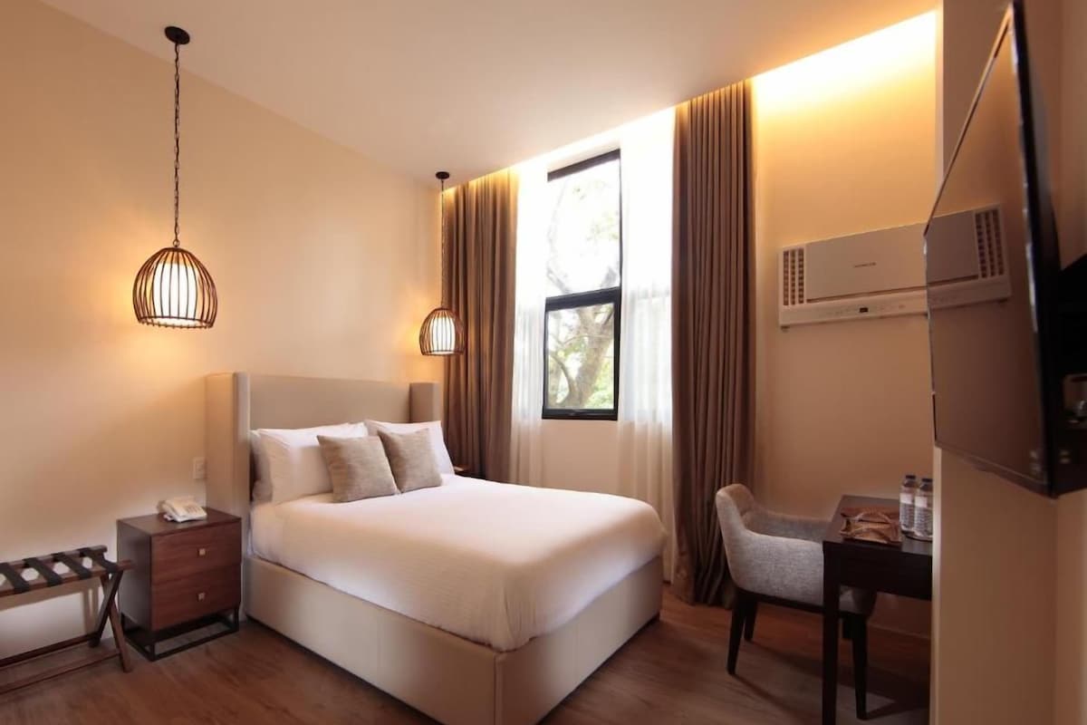 Quarto de hotel com cama, mesa de cabeceira, abajur, cadeira e escrivaninha com cadeira.