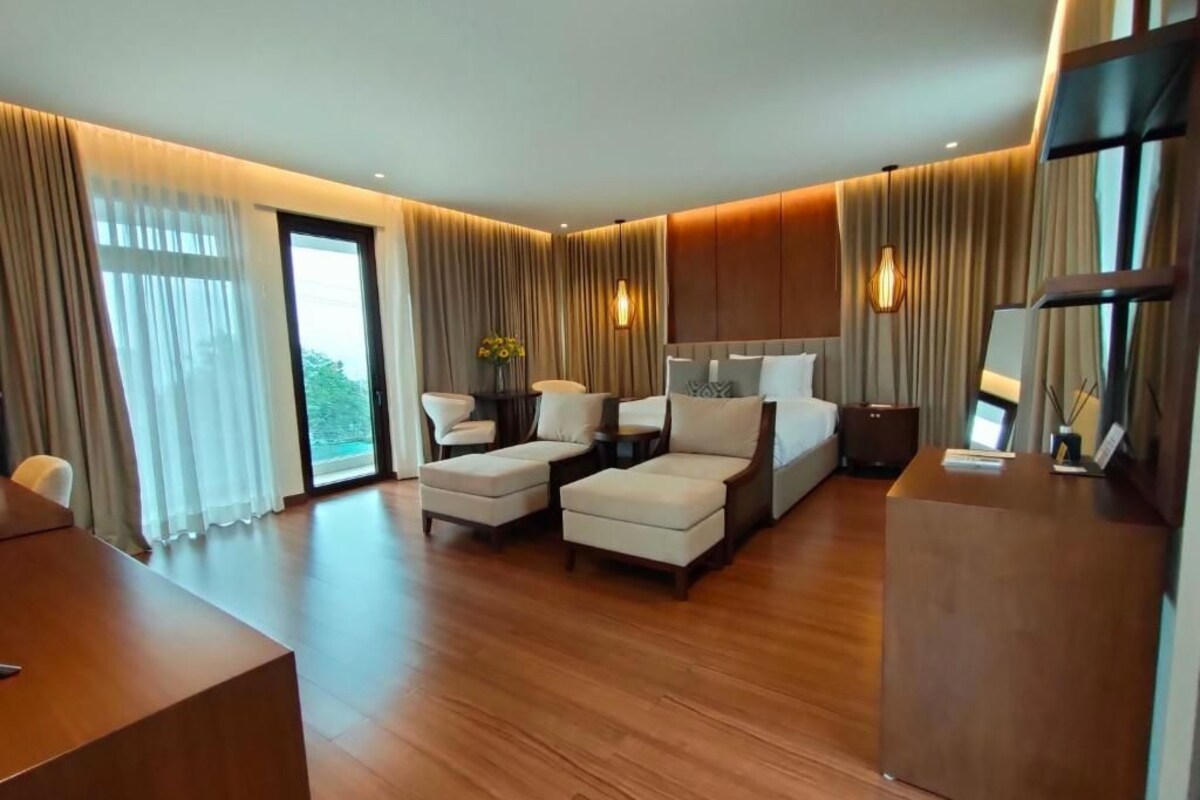 Quarto de hotel moderno com uma cama grande, duas poltronas, uma escrivaninha e uma televisão.