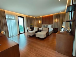 Quarto de hotel moderno com uma cama grande, duas poltronas, uma escrivaninha e uma televisão.