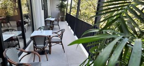 A balcony with tables and chairs, potted plants, and a view of trees. - Girasol Tagaytay (Alfonso)