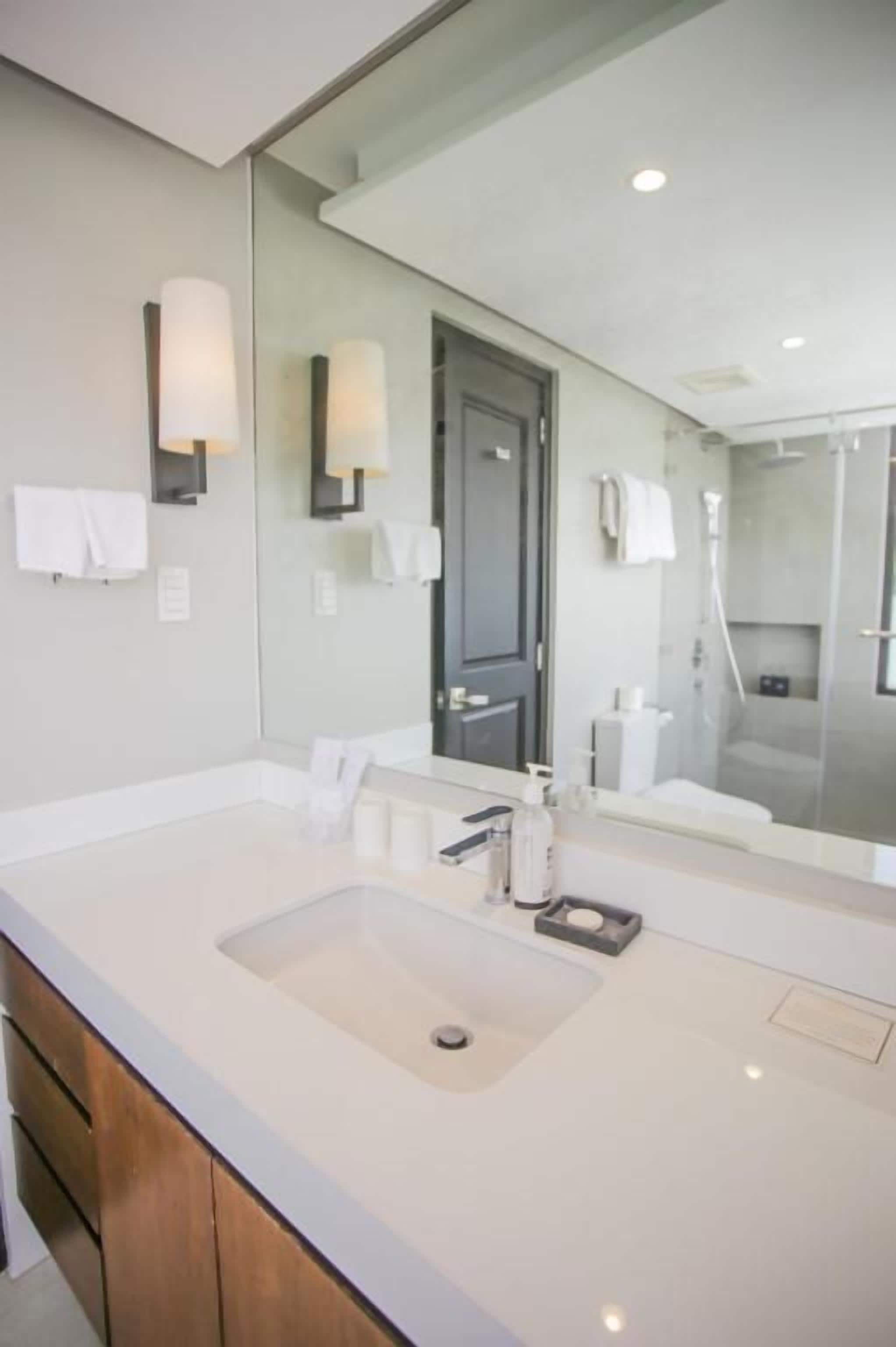 Un baño moderno con un espejo grande, un lavamanos y una zona de ducha.