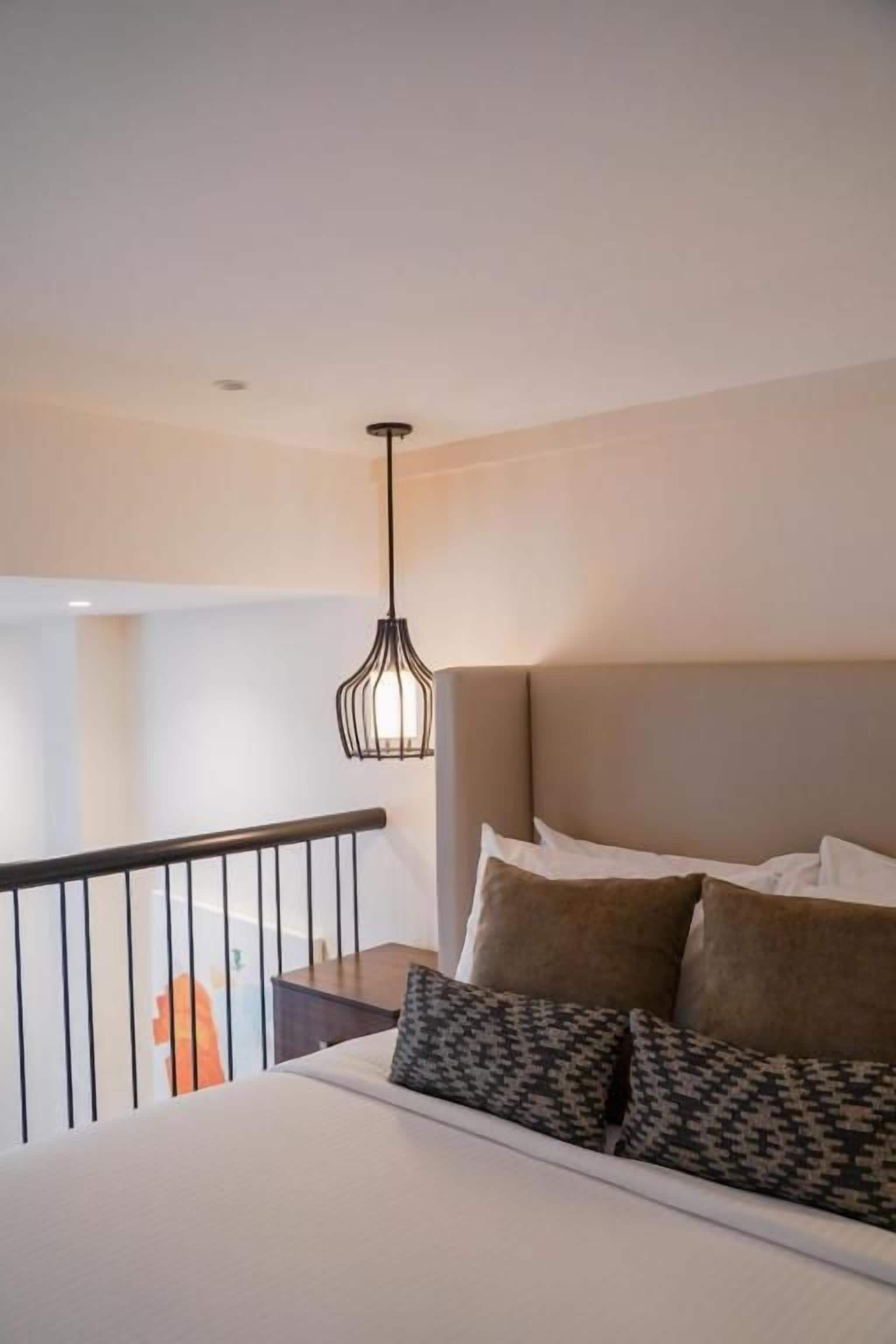 A hotel room with a bed, a hanging light fixture, and a view of the outside.