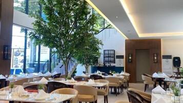 A modern restaurant interior with multiple dining tables, chairs, and a central tree.