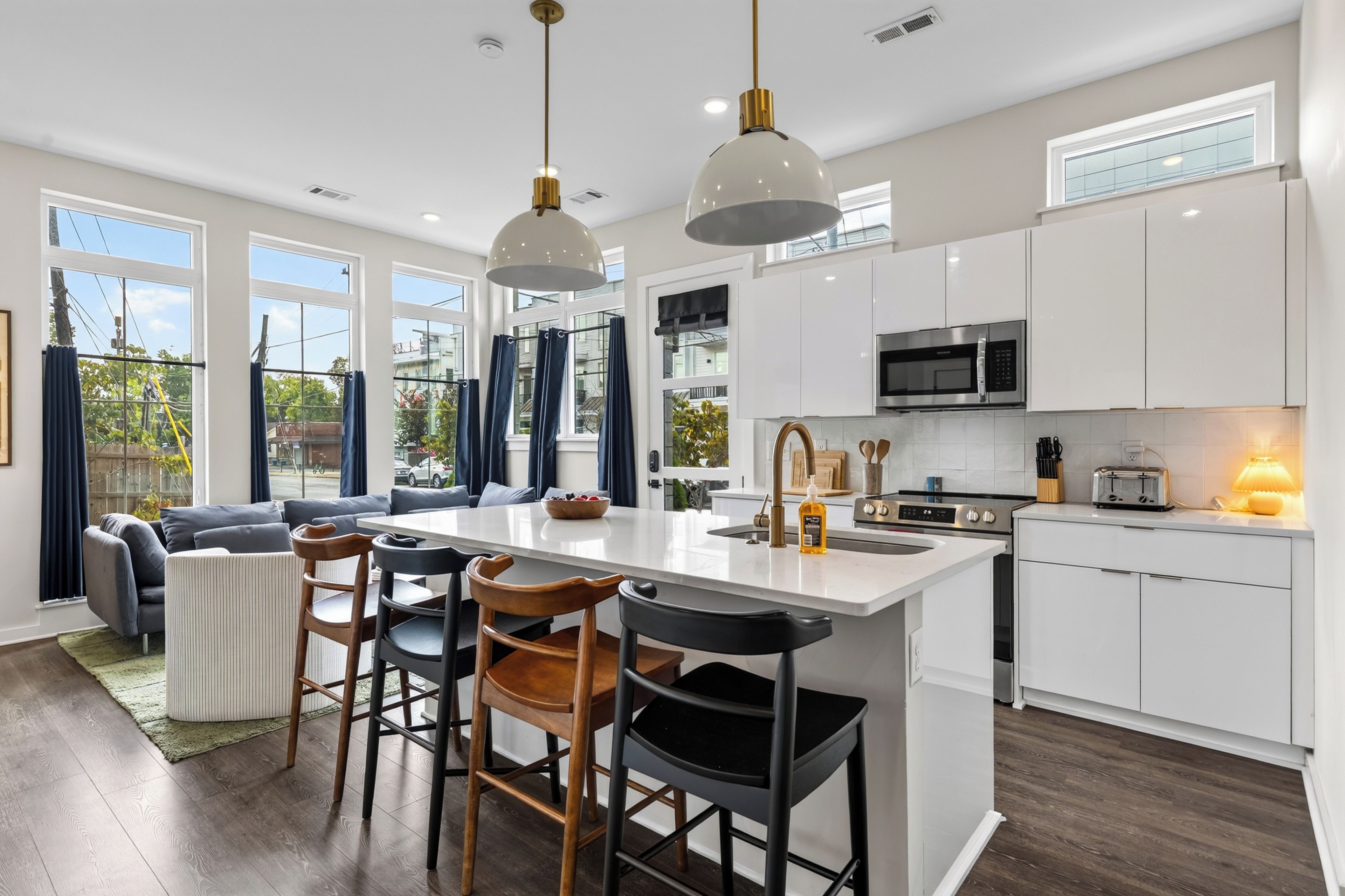 A modern kitchen with a central island, bar stools, and a dining area with a sofa and chairs.