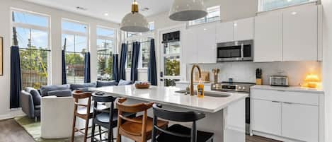 Una cocina moderna con una isla central, taburetes de bar y un comedor con sofá y sillas.