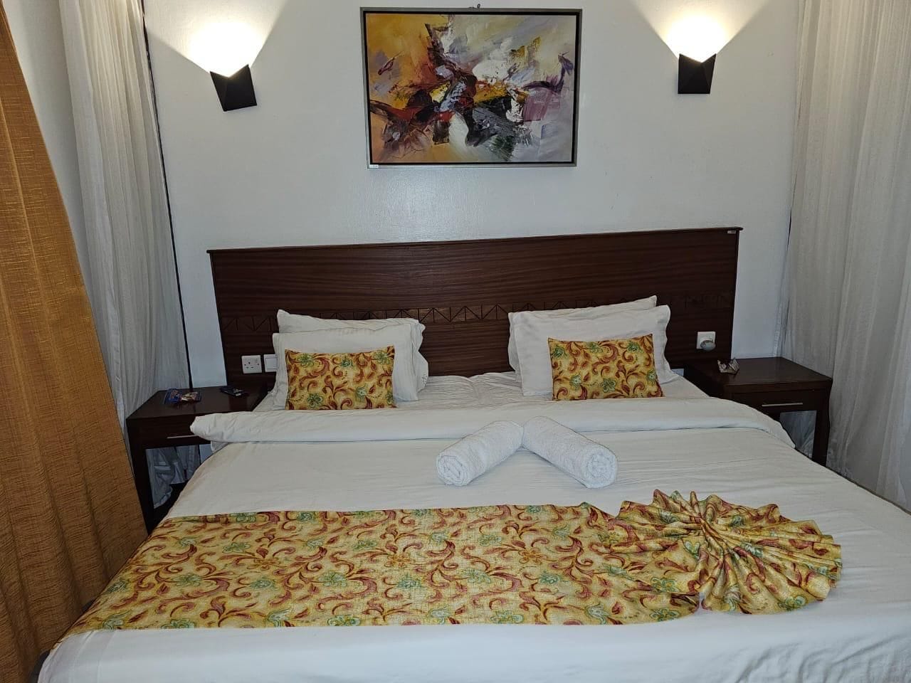 Een hotelkamer met een groot bed, twee nachtkastjes, een hoofdbord en een abstract schilderij aan de muur.