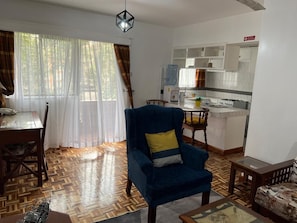 Uma sala de estar com uma poltrona azul, uma mesa de jantar e uma cozinha com armários brancos e um dispensador de água.