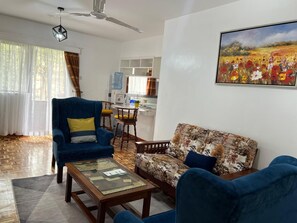 Een woonkamer met een bank, fauteuil en salontafel. Er is een eethoek met stoelen en een tafel. Aan de muur hangt een schilderij.