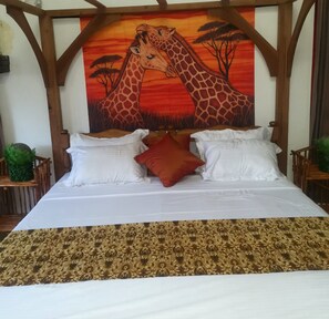 Ein Bett mit weißer Bettwäsche und einem gemusterten Überwurf, flankiert von zwei Nachttischen mit grünen Pflanzen, unter einer großen Giraffen-Mural.