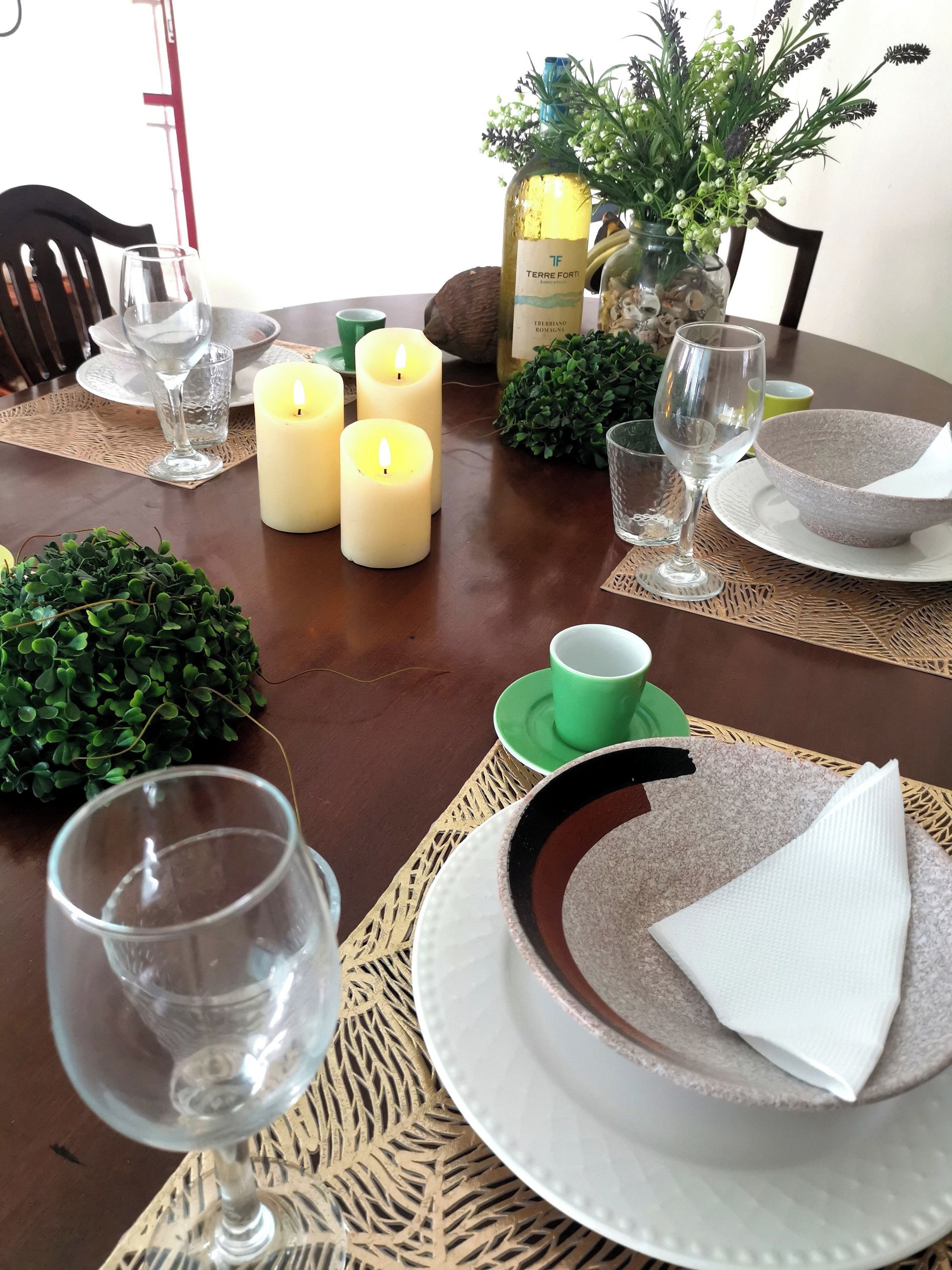 Un tavolo da pranzo apparecchiato con candele, bicchieri e un centrotavola decorato con elementi verdi.