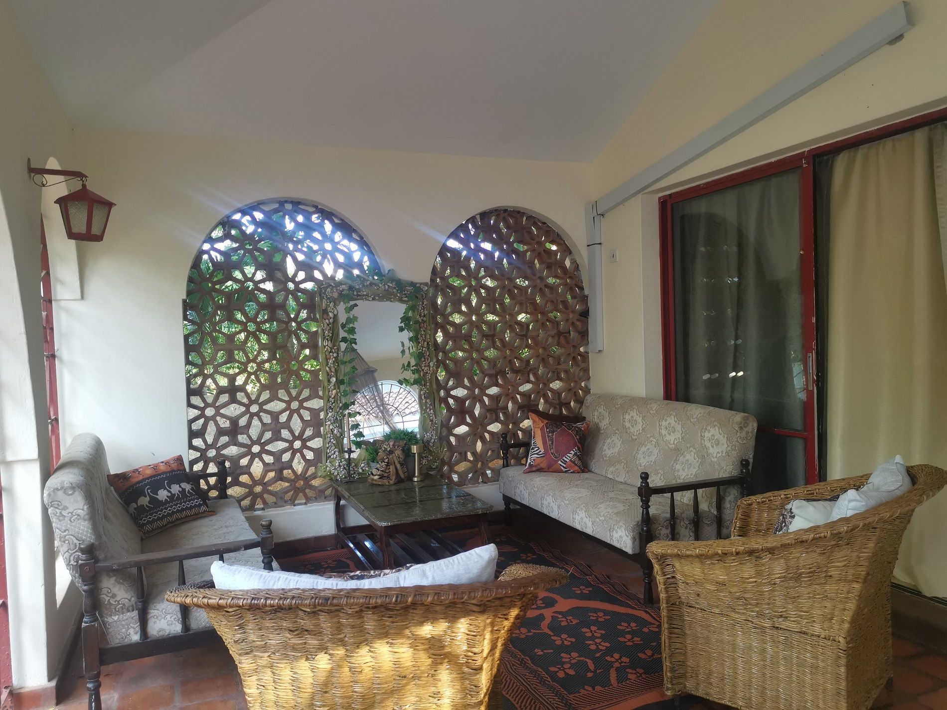 A cozy living area with a sofa, two wicker chairs, a coffee table, and decorative elements like a lattice screen and a lantern.
