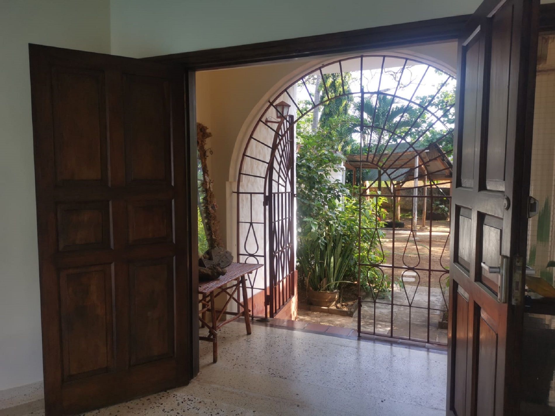 An open wooden door leading to a covered outdoor area with a bench and potted plants.