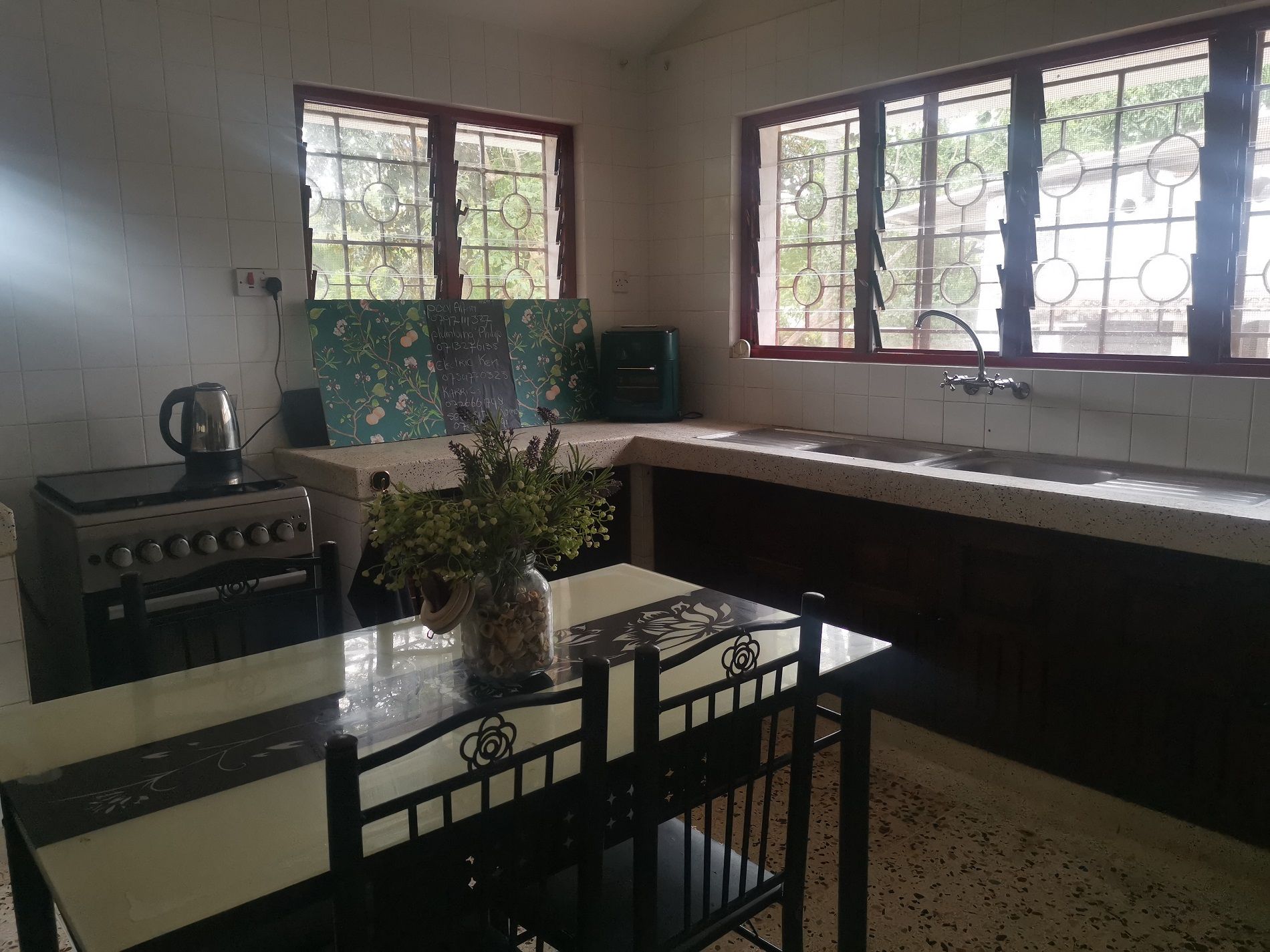 A kitchen with a gas stove, a sink, a window with a view of greenery, and a table with chairs.