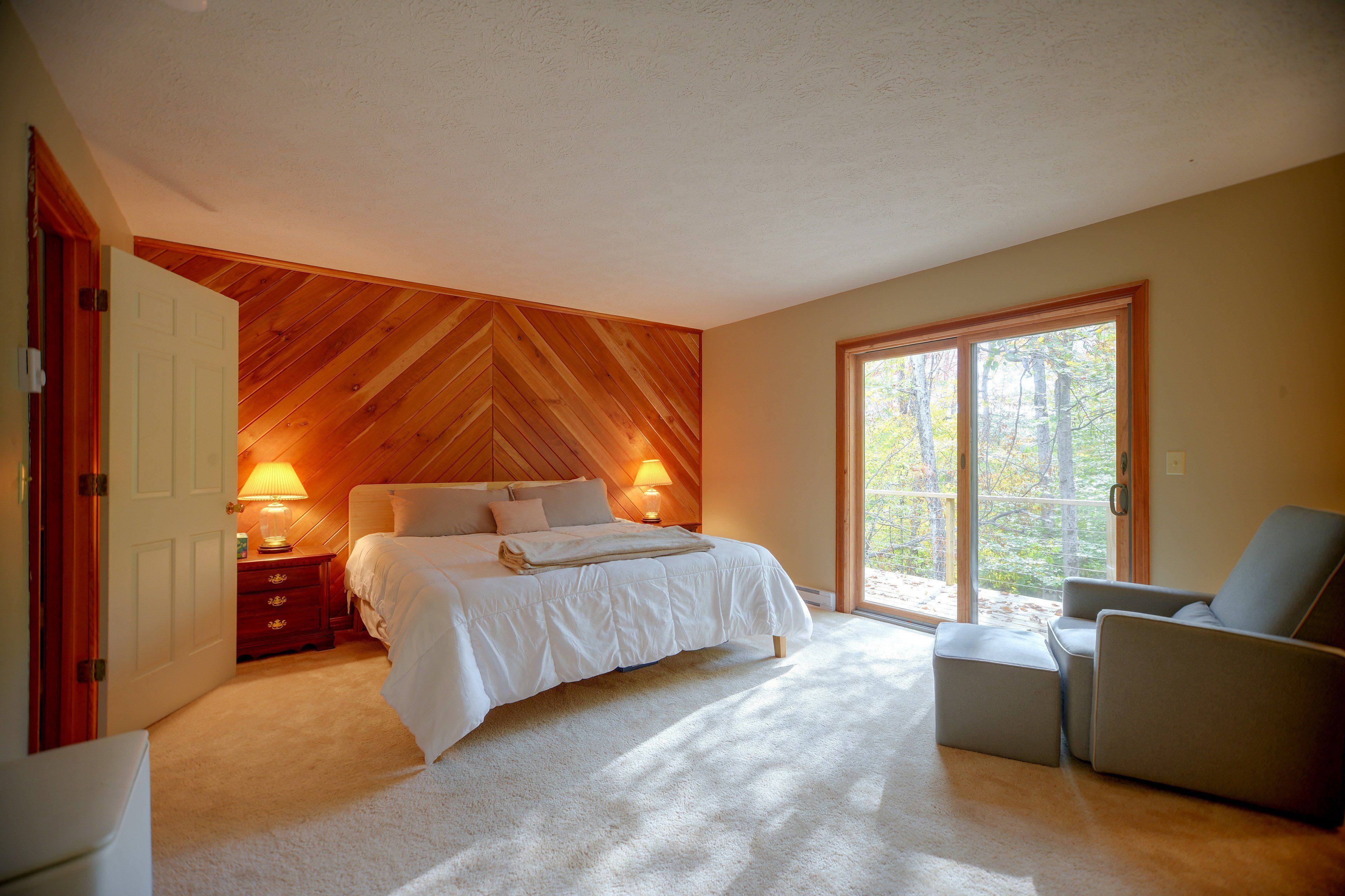 A bedroom with a bed, bedside lamps, a chair, and a view through a door.