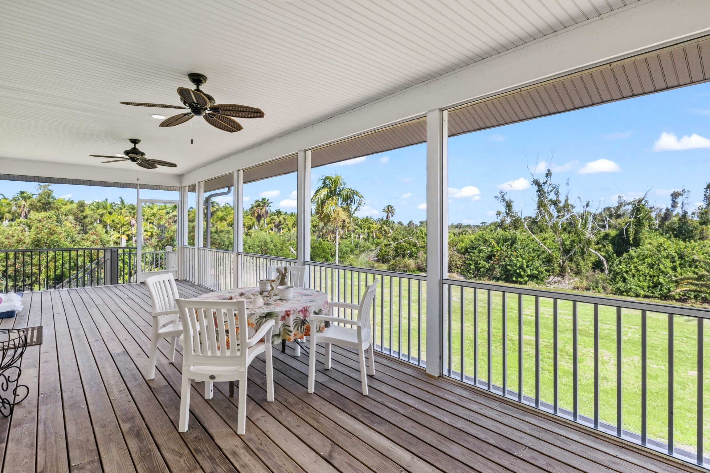 A covered outdoor area with a table and chairs, a ceiling fan, and a view of a green landscape.