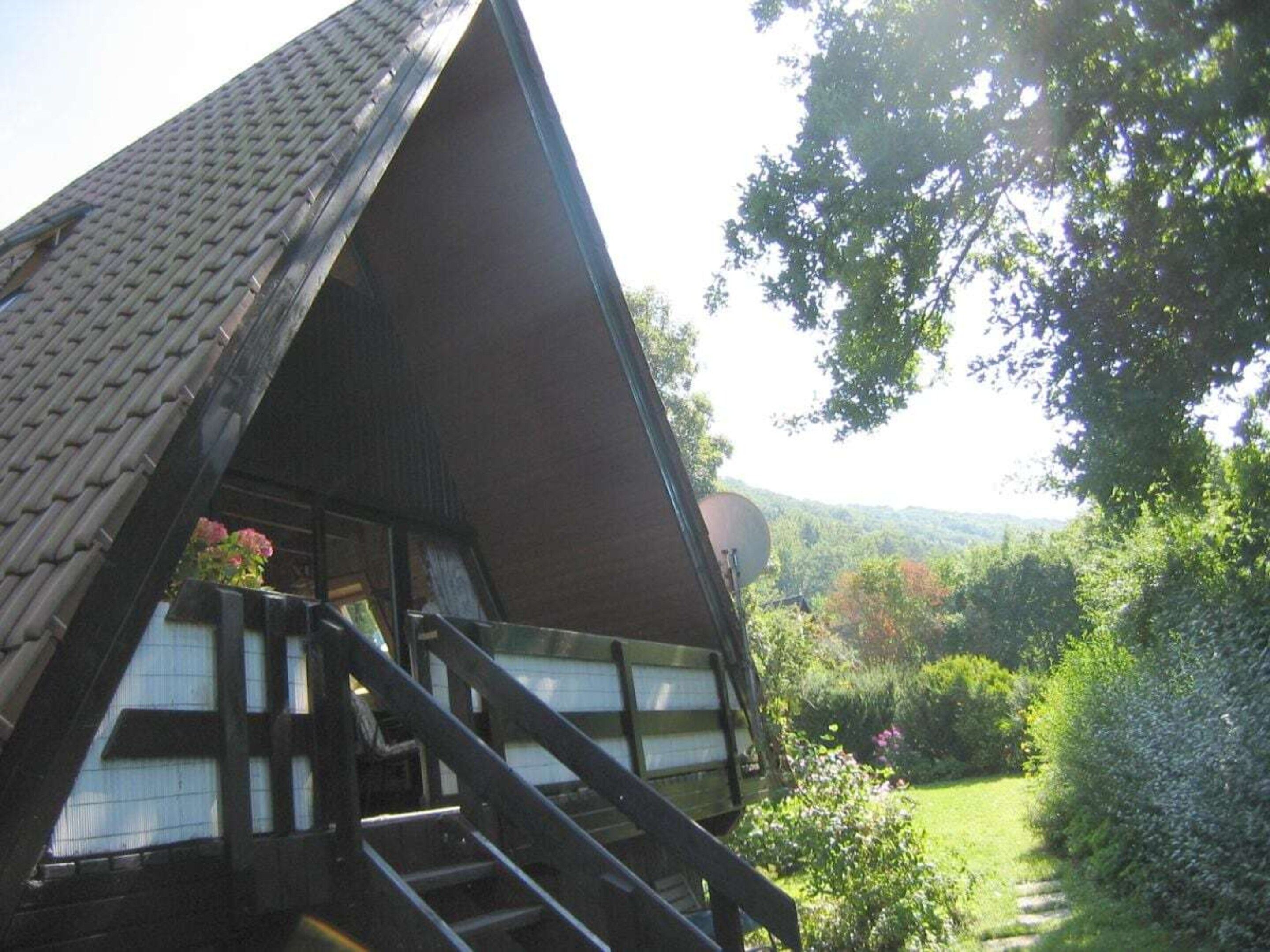 A traditional chalet with a steeply pitched roof, wooden staircase, and a view of a lush garden.