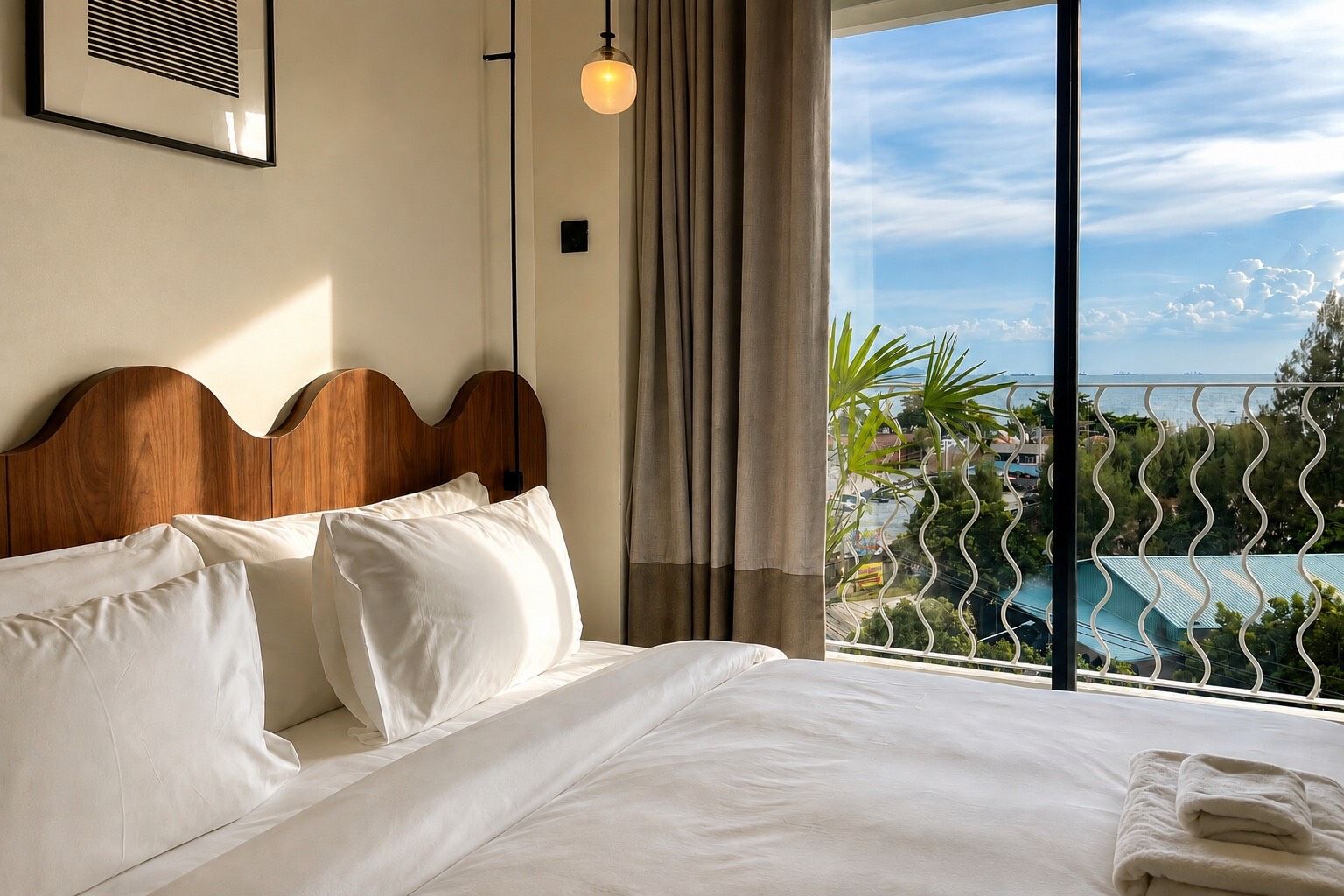 A hotel room with a large bed, a wooden headboard, a view of a pool and buildings, and a balcony with a railing.