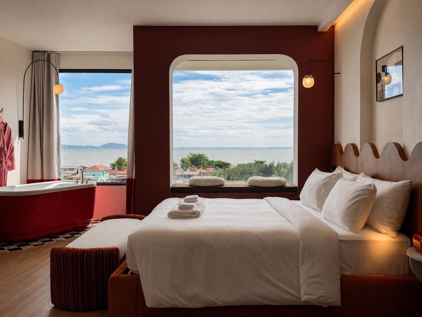 Habitación de hotel con un ventanal grande, una cama con ropa blanca, una silla roja y una bañera.