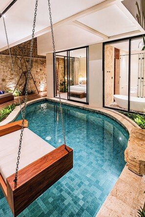 Een modern binnenzwembad met een hangstoel, een slaapkamer met glazen wanden en een aparte badkamer.