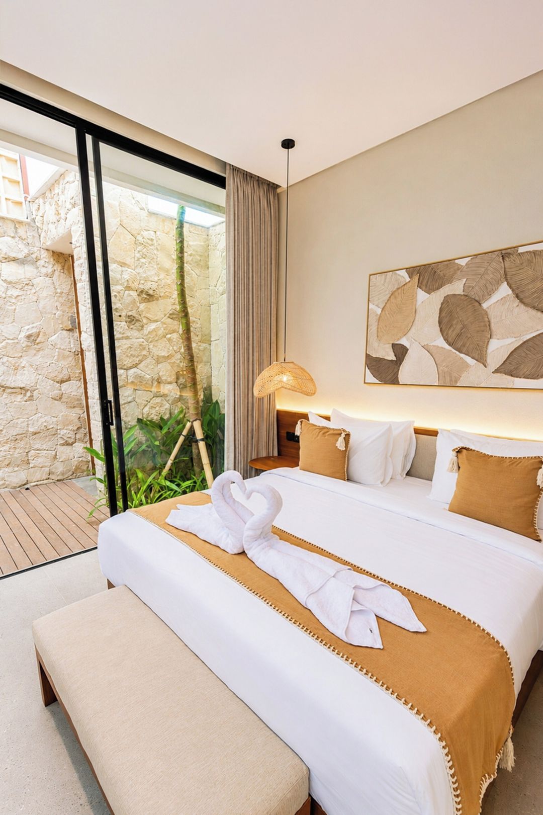Een hotelkamer met een bed, een bankje, een lamp en uitzicht op een stenen muur en groen.