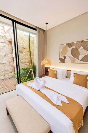 Een hotelkamer met een bed, een bankje, een lamp en uitzicht op een stenen muur en groen.