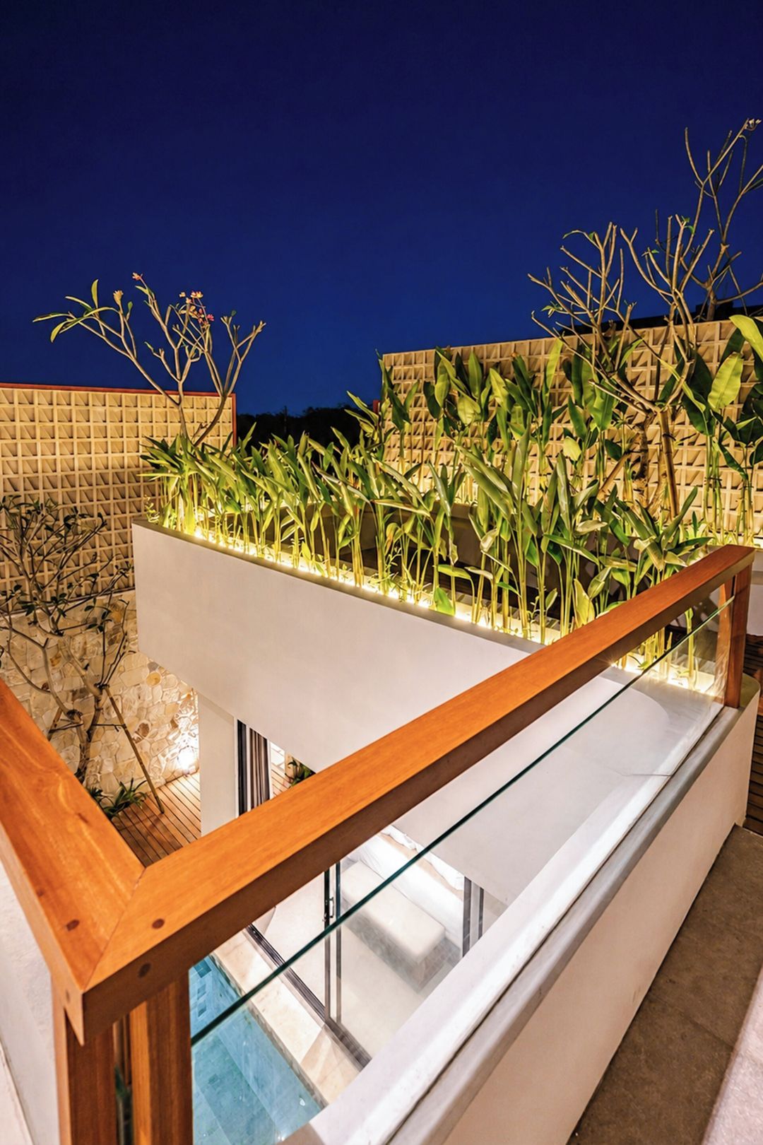 Een modern balkon met glazen hekwerk, een stenen muur en verschillende planten.