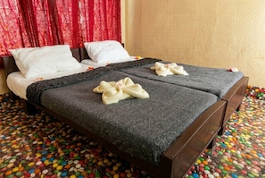 Una cama doble con colcha gris y almohadas blancas, una cortina roja al fondo, y un suelo cubierto de caramelos de colores.