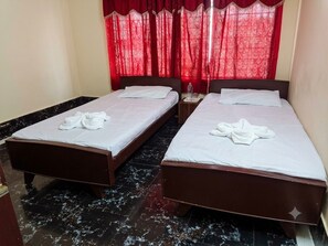 Habitación de hotel con dos camas, cada una con una toalla doblada y una mesita entre ellas.