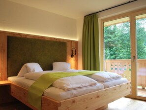 Ein hölzernes Bett mit grüner Decke, ein Holz-Kopfstück und Blick ins Grüne durch eine Schiebetür.