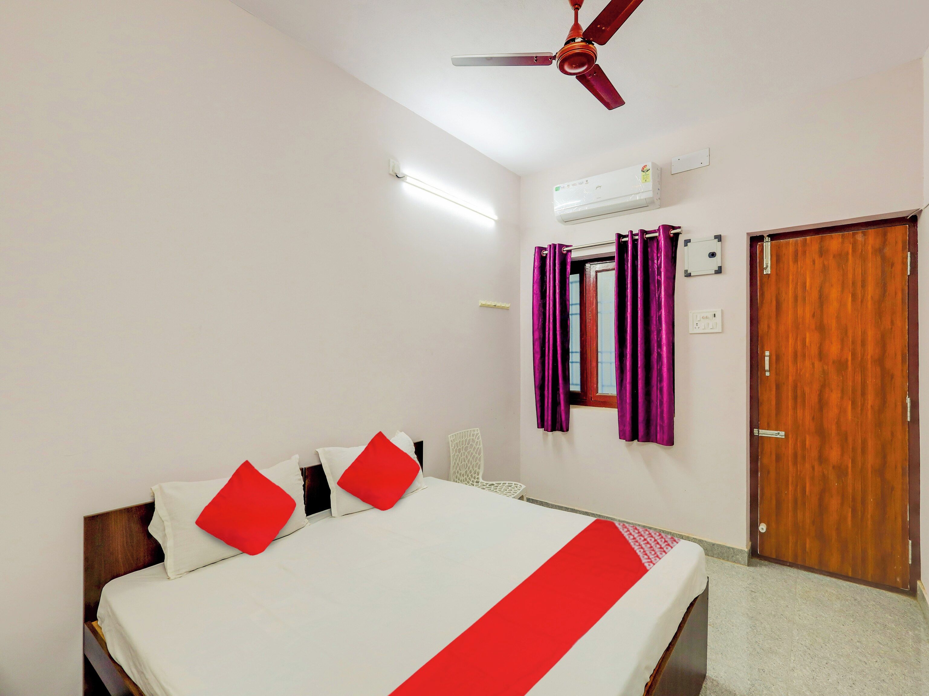 A hotel room with a bed, a ceiling fan, an air conditioning unit, a wooden door, and purple curtains.